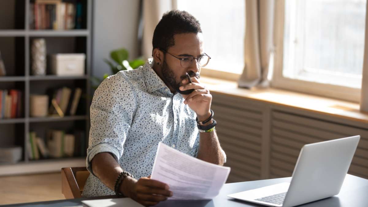 Focused serious african american businessman accountant analyst holding documents looking at laptop computer screen